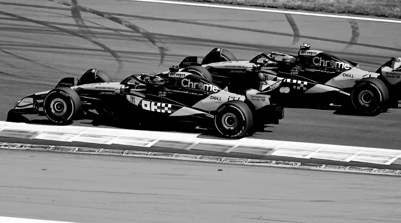 Two Formula 1 cars racing wheel to wheel, both covered in sponsor logos